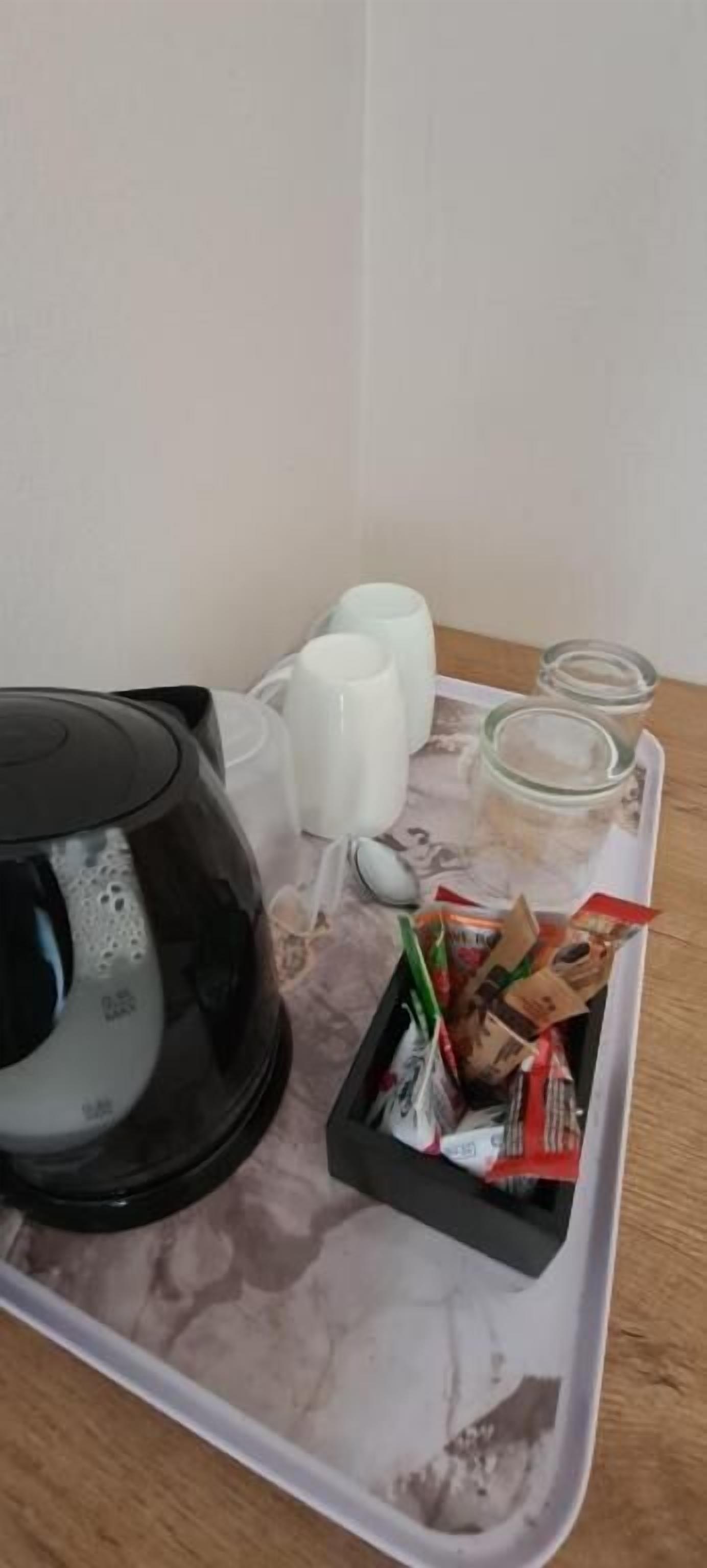 A tray with a coffee maker, cups, and a container of snacks.