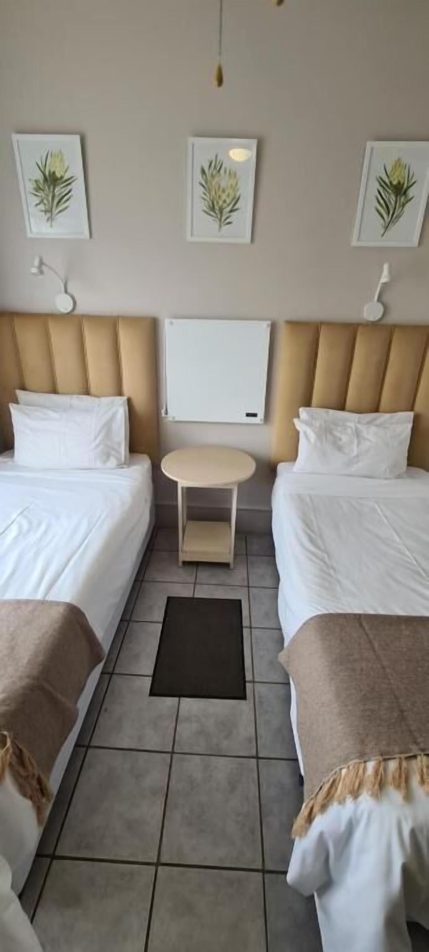Habitación de hotel con dos camas, una mesita y obras de arte en las paredes.