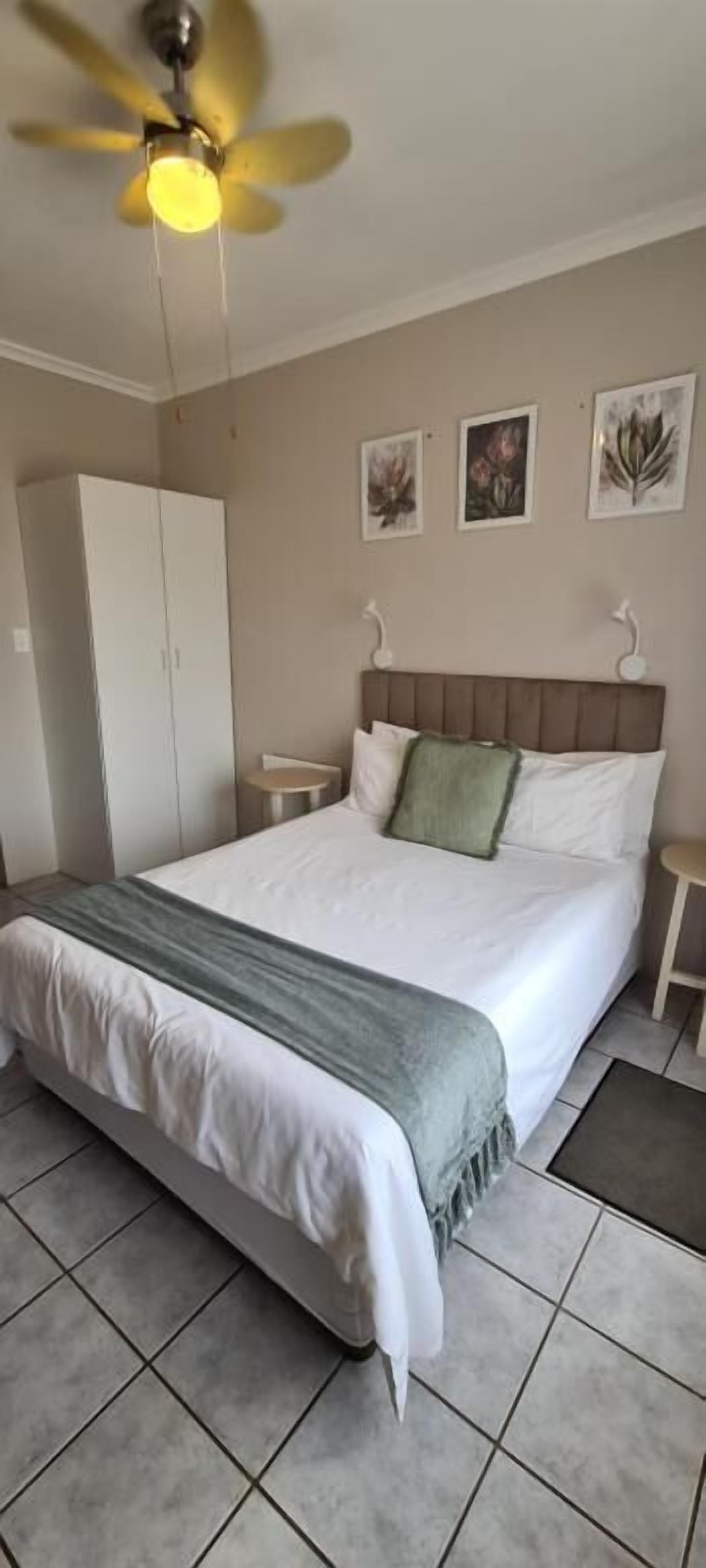 A bedroom with a bed, a ceiling fan, a wardrobe, and artwork on the wall.