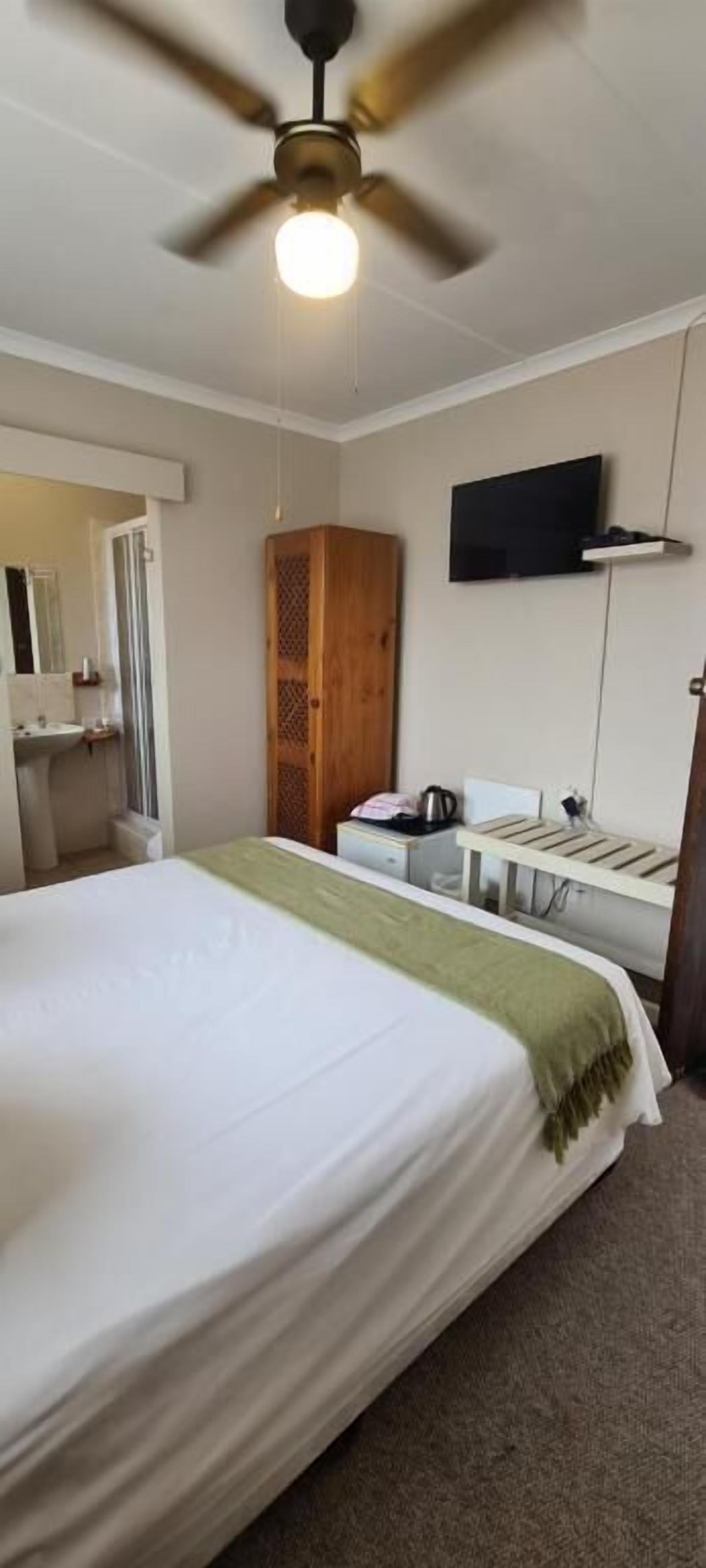 Una habitación de hotel con una cama, un ventilador de techo, un televisor y un armario de madera.