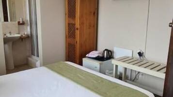 Una habitación de hotel con una cama, un ventilador de techo, un televisor y un armario de madera.