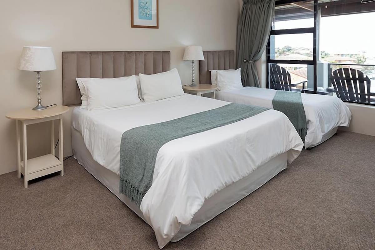 A hotel room with two beds, a view of the city, and a balcony with chairs.