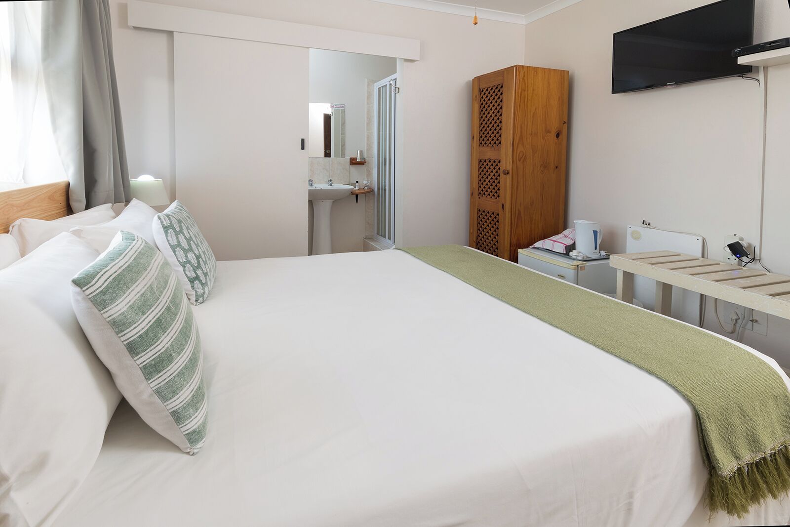 Ein Hotelzimmer mit Bett, Fernseher, Schreibtisch mit Computer und einer Duschkabine.
