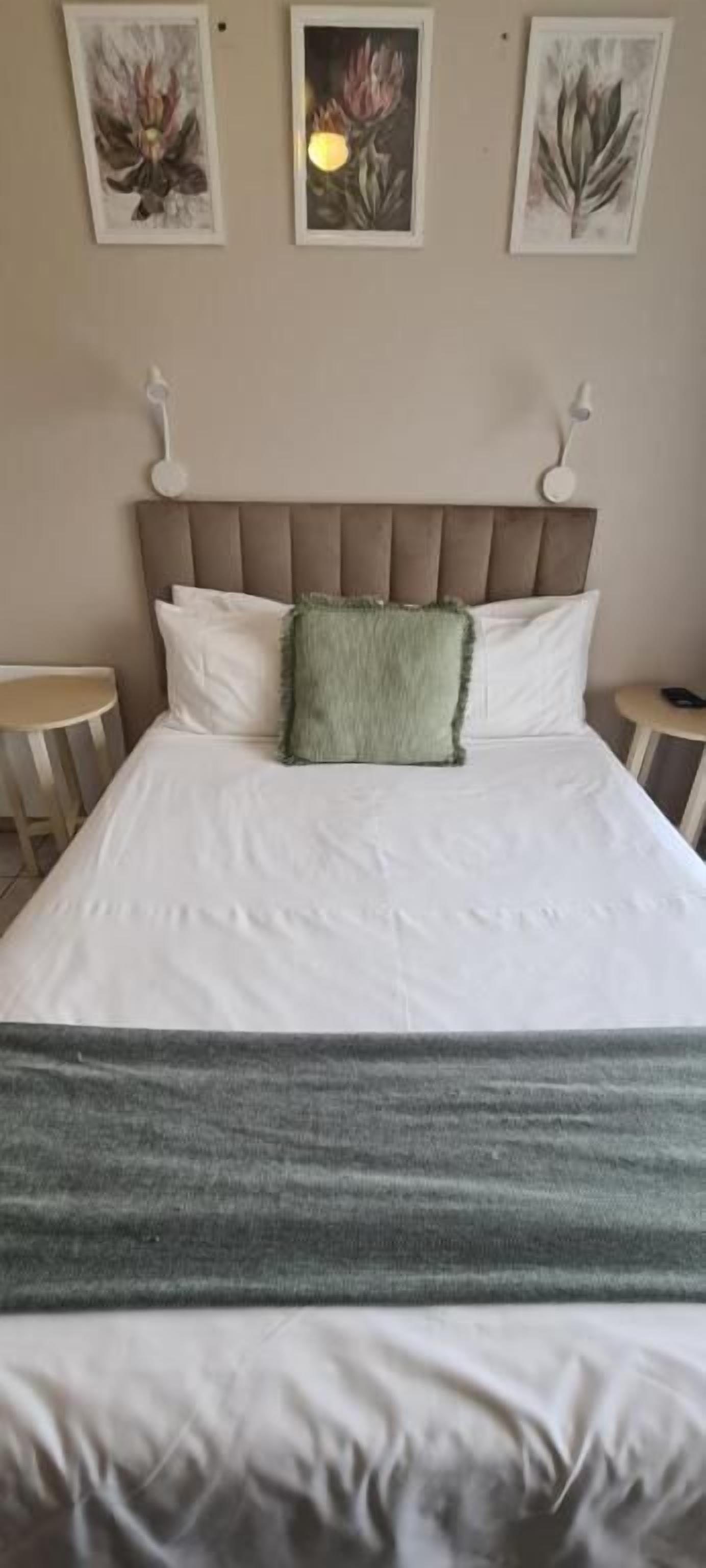 A bed with a headboard, two bedside tables, and three framed botanical prints on the wall.