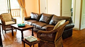 A living room with a leather sofa, wicker chairs, a wooden coffee table, and a door in the background. - Magoebaskloof Getaway (Tzaneen)