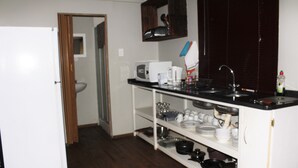 A compact kitchen with a microwave, sink, and shelves for dishes and cookware. - Magoebaskloof Getaway (Tzaneen)