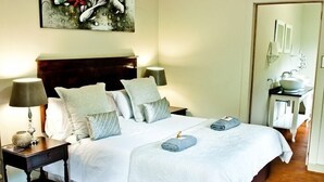 A neatly made bed with a white comforter, two pillows, and a folded towel. There is a nightstand with a lamp and a decorative item beside the bed. - Magoebaskloof Getaway (Tzaneen)