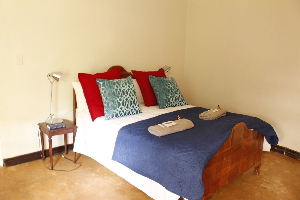 Un lit bien fait, avec une couvre-lit bleue, des oreillers rouges et turquoise, et une tête de lit en bois.