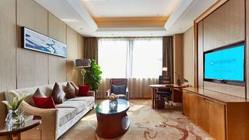A hotel room with a sofa, coffee table, TV, and a large window with curtains.