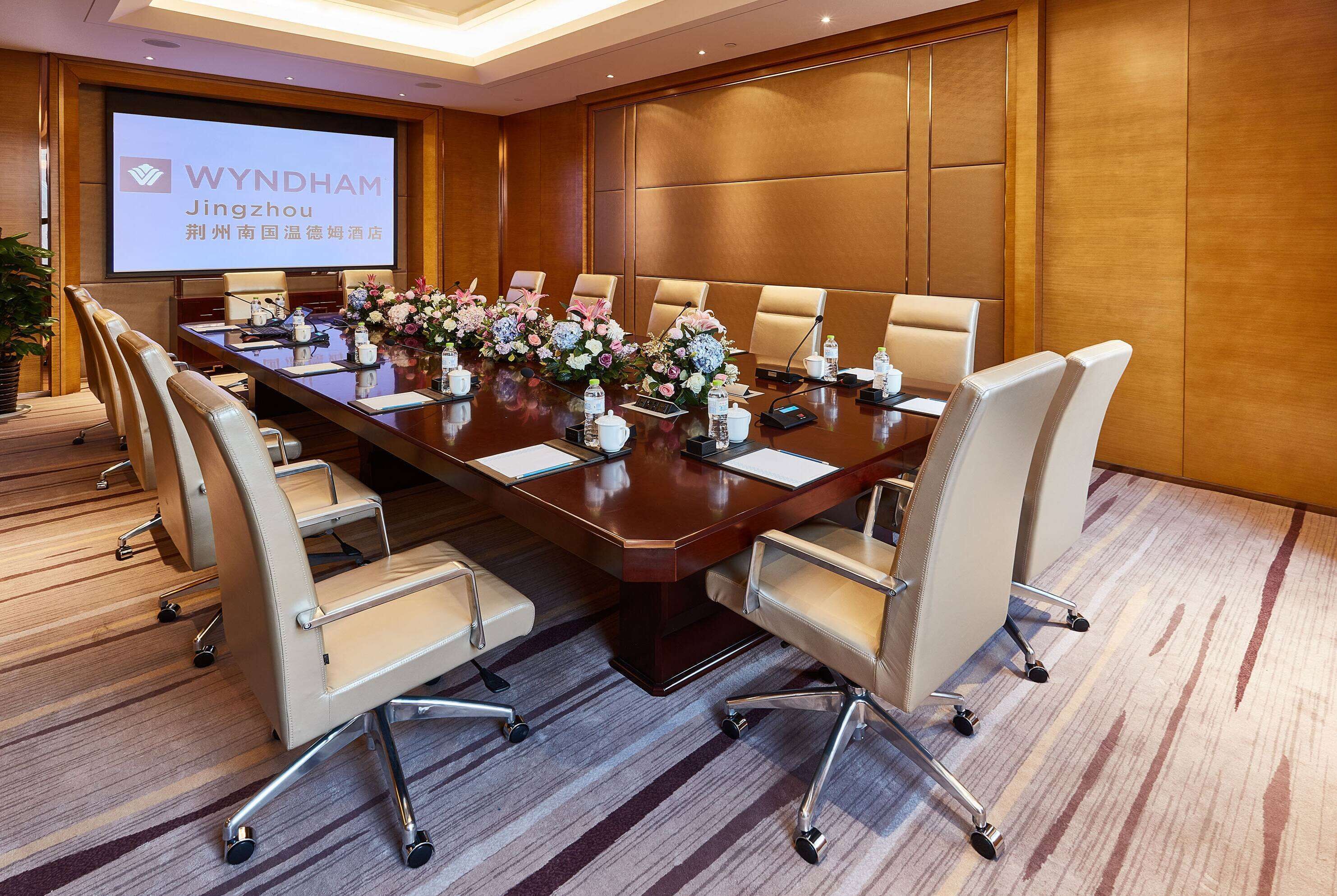 A conference room with a long table, chairs, a projector screen, and floral centerpieces.