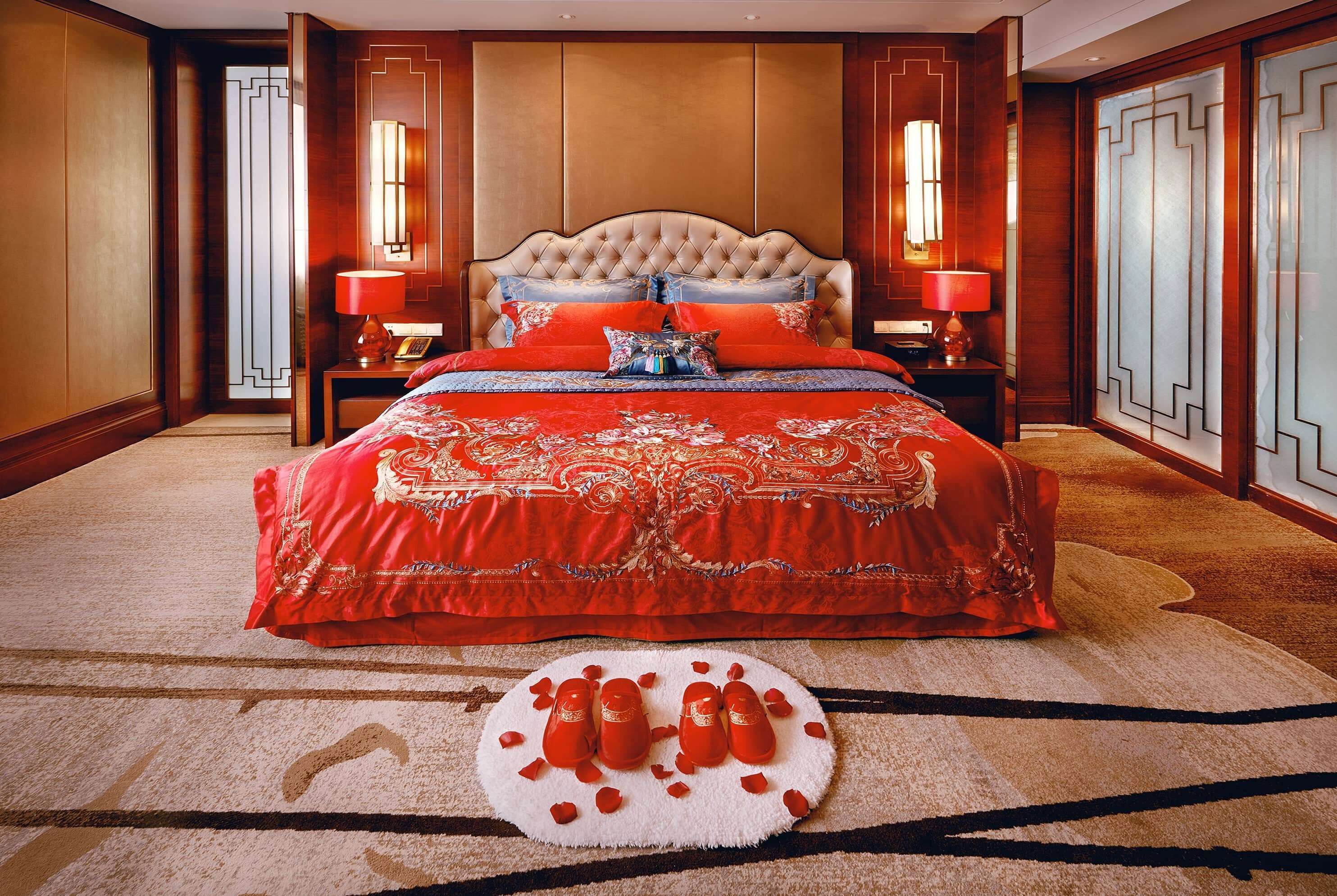 A large bed with a tufted headboard, two bedside tables with lamps, and a decorative rug with a circular pattern.