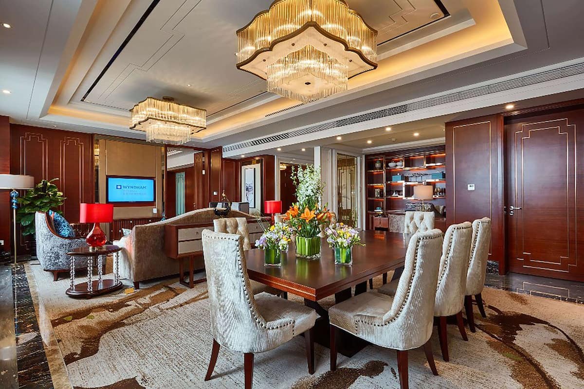 A spacious dining area with a large wooden table, upholstered chairs, and a chandelier.
