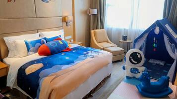 A hotel room with a bed featuring a space-themed bedspread, a plush astronaut toy, a blue rocking horse, and a small play tent.