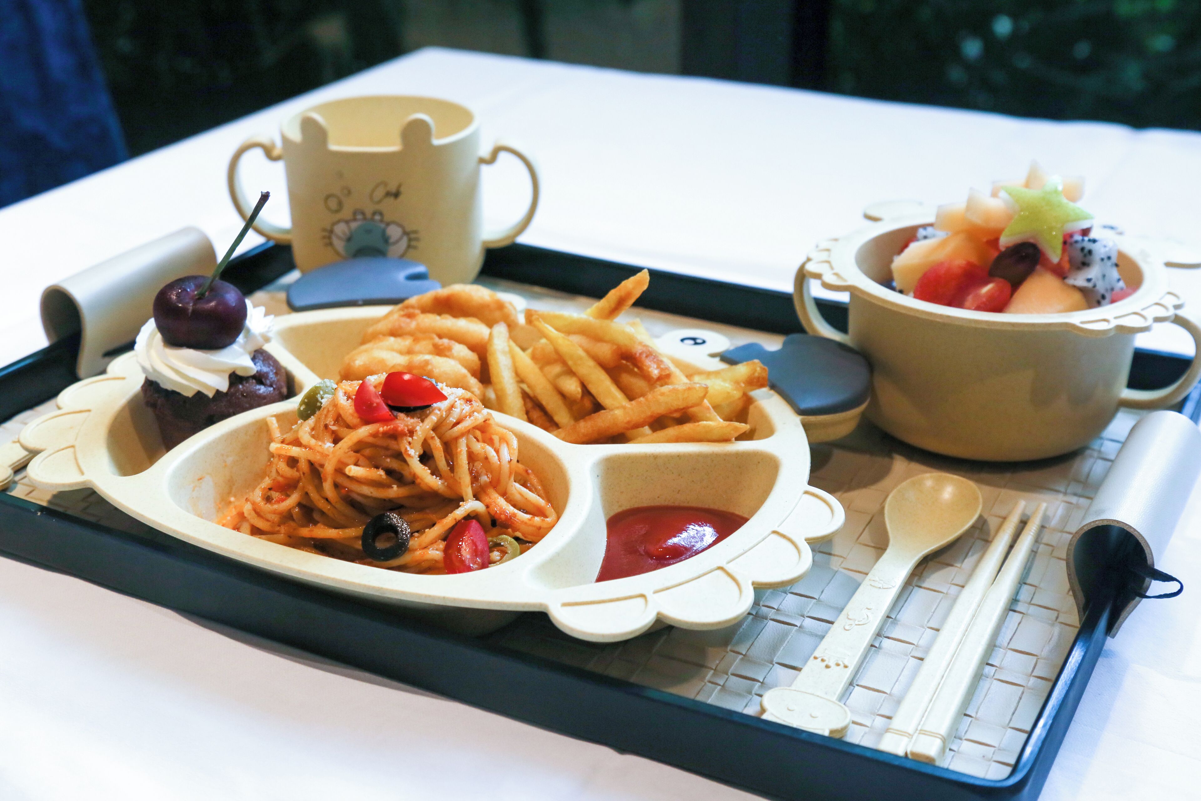 Eine Schale mit Spaghetti, Pommes, einer Kirsche und einer Obstschale.