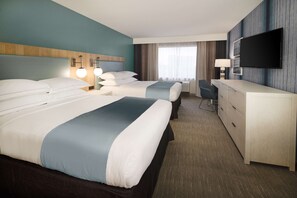 A hotel room with two beds, a desk, a television, and a large window with curtains.