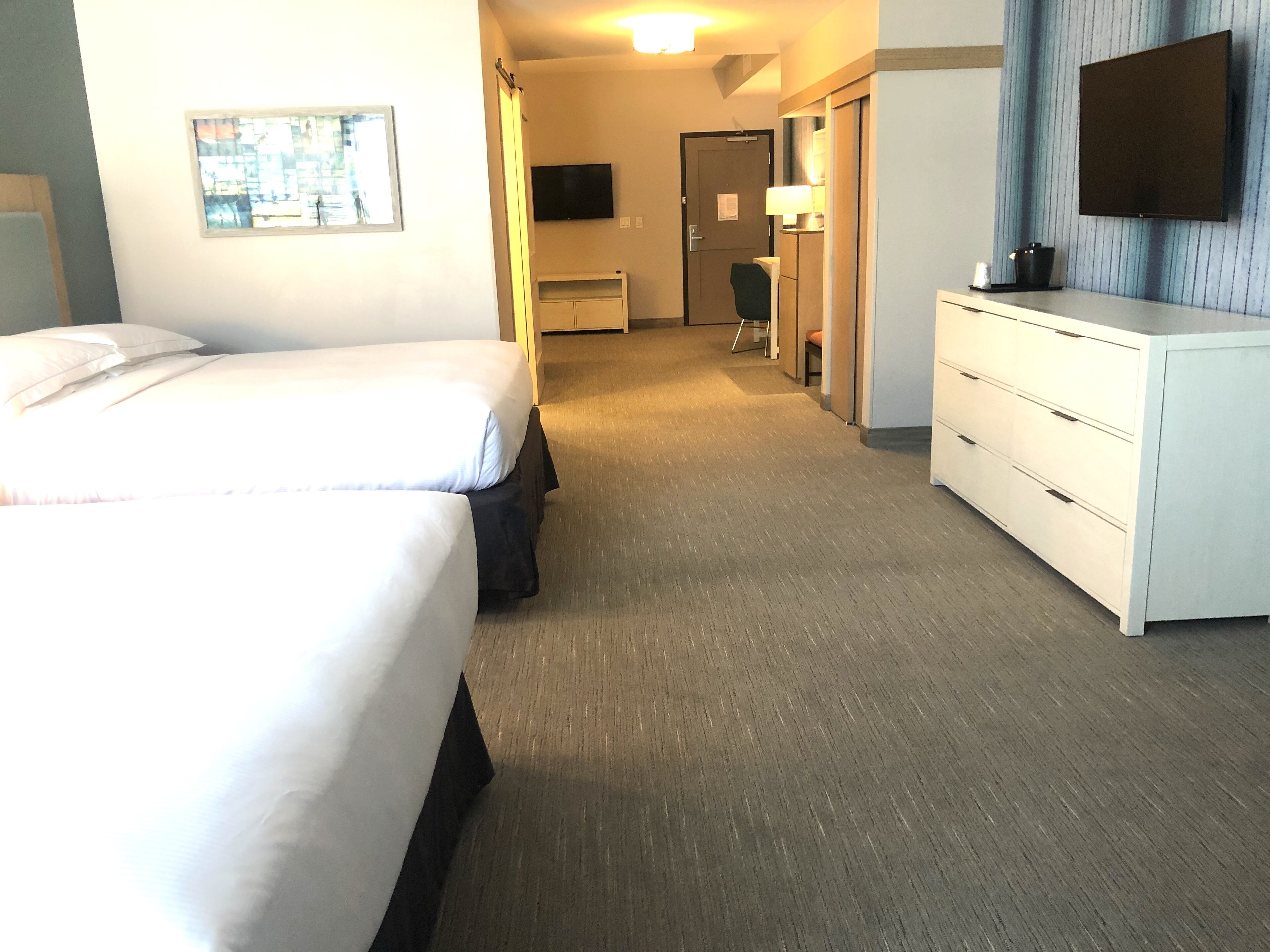 A hotel room with a large bed, a desk, a chair, a TV, and a dresser.