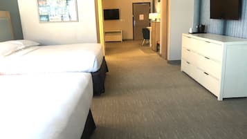 A hotel room with a large bed, a desk, a chair, a TV, and a dresser.