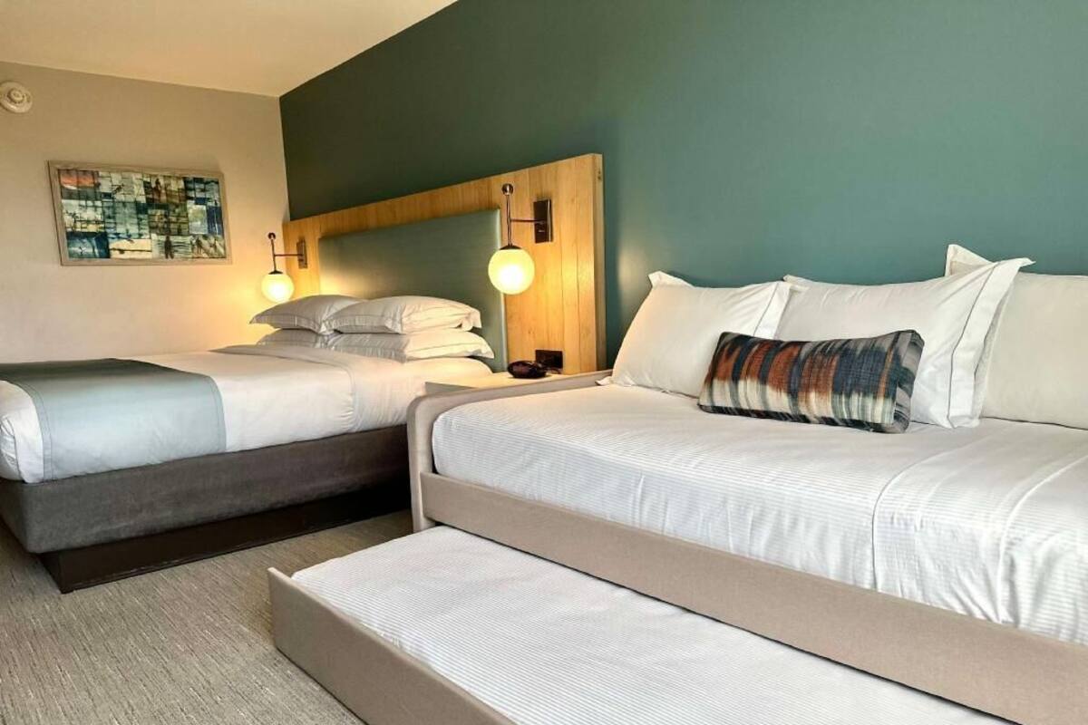 A hotel room with two beds, a headboard, bedside lamps, and a wall-mounted artwork.