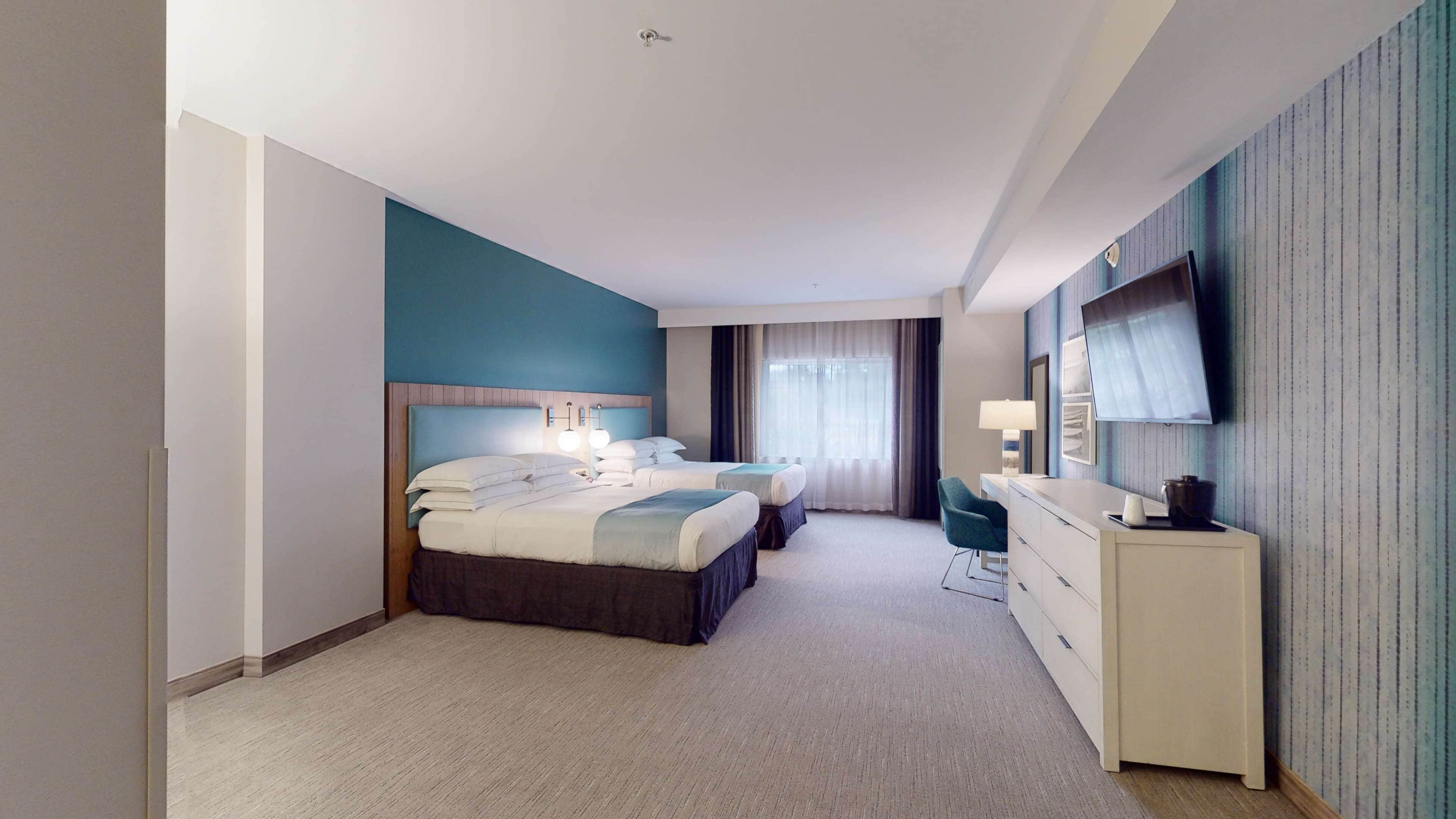 A modern hotel room with a large bed, a desk, a chair, and a TV mounted on the wall.