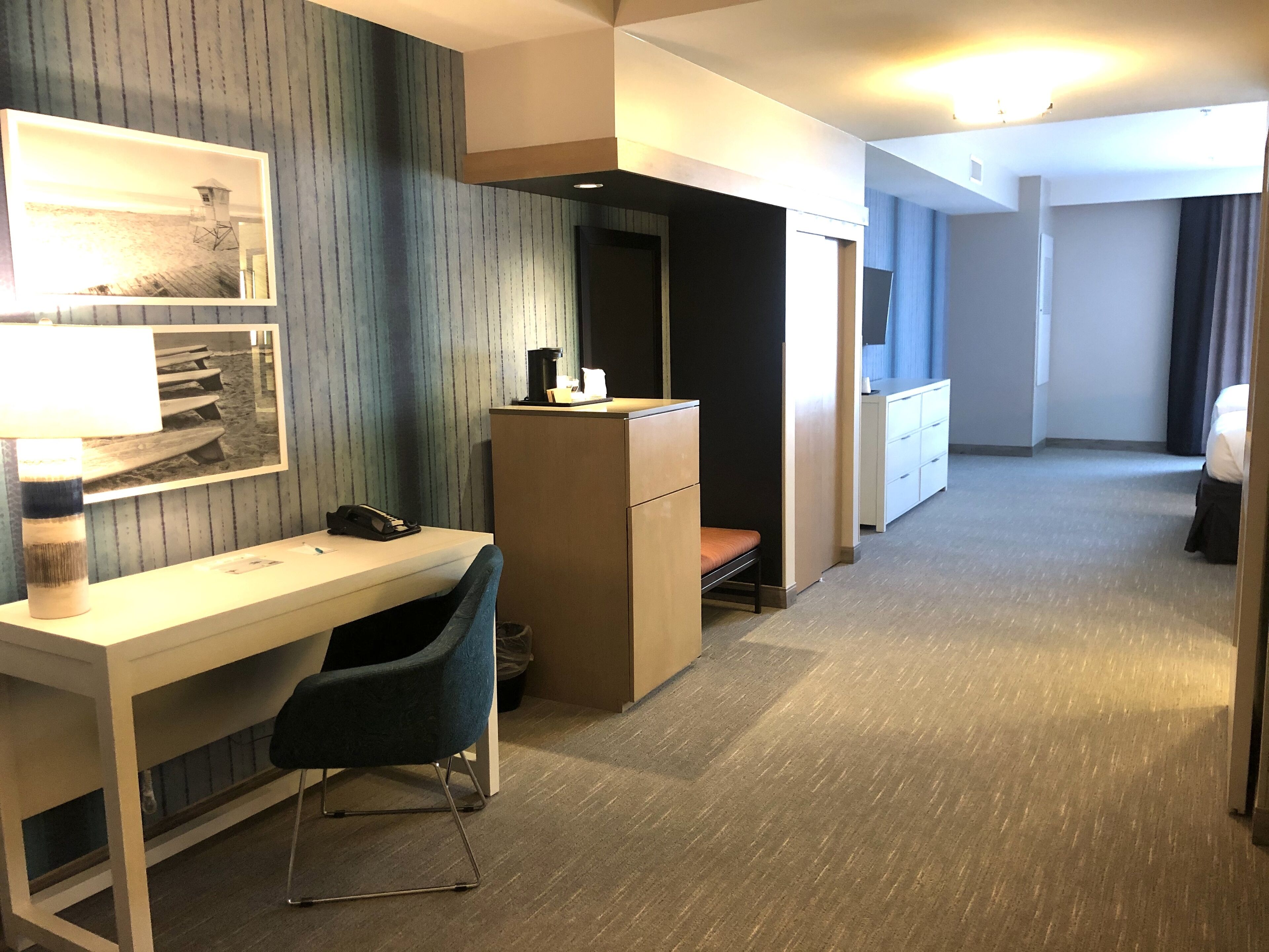 A hotel room with a desk, chair, and a bed.