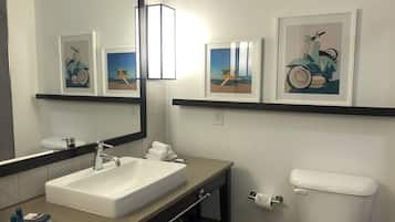 Un baño moderno con un espejo grande, un lavabo, un inodoro y obras de arte enmarcadas en las paredes.