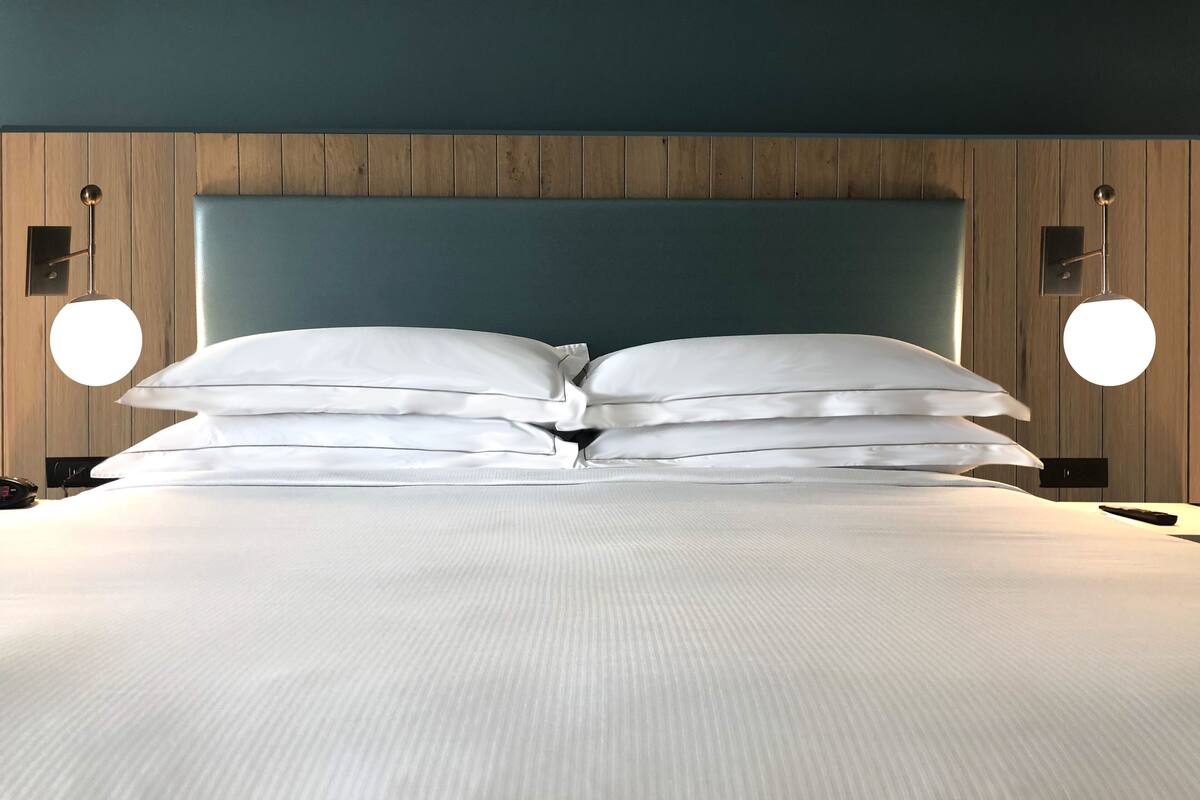 A neatly made bed with white linens and two round wall sconces on either side.