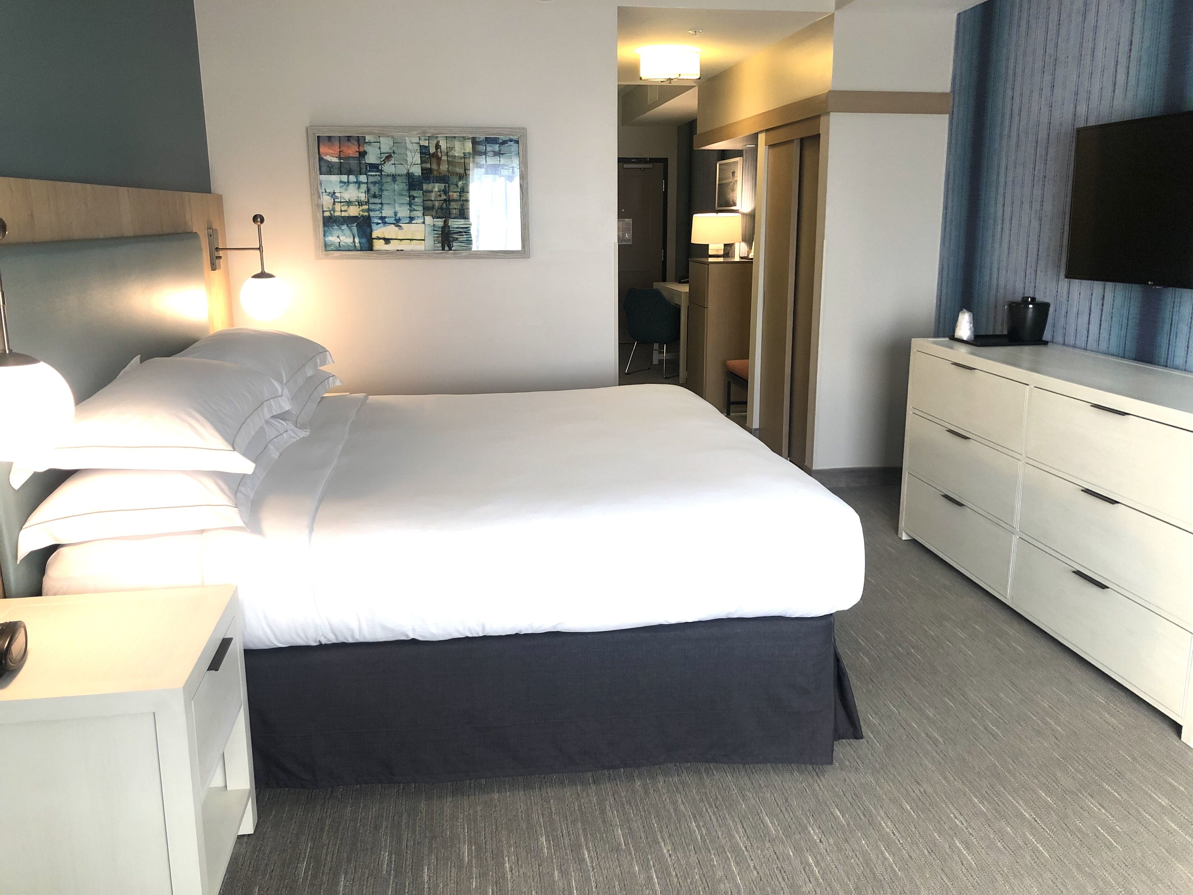 A hotel room with a large bed, bedside tables, a flat-screen TV, and a painting on the wall.