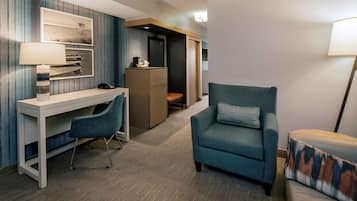 Una habitación de hotel con escritorio, un sillón azul, sofá, lámpara y estantería.