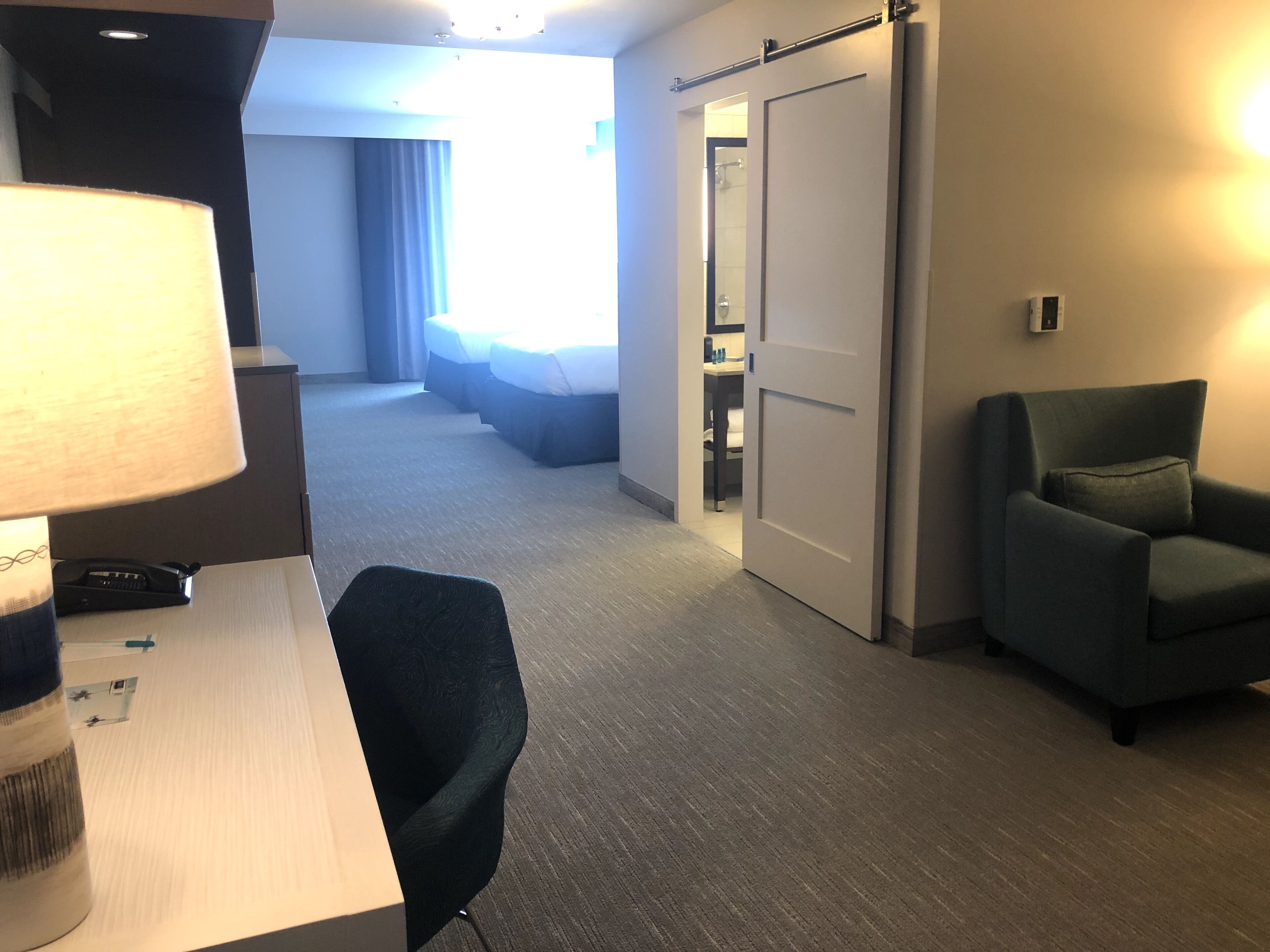 A hotel room with a desk, chair, bed, and a sliding door leading to a bathroom.