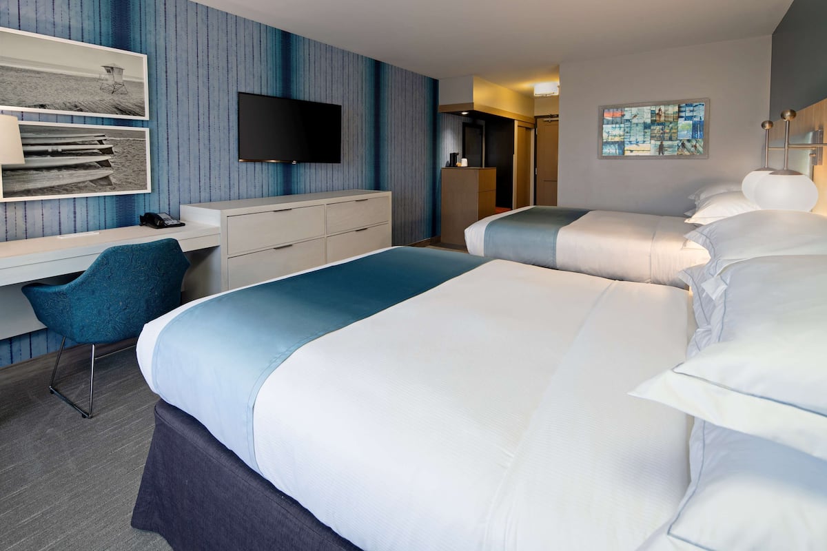 A hotel room with two beds, a desk with a chair, a TV, and artwork on the walls.