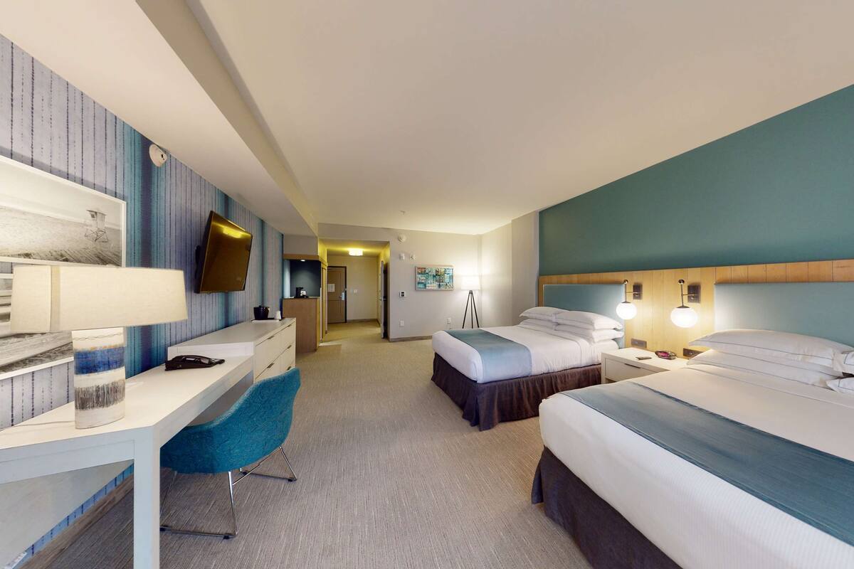 A hotel room with a desk, two beds, a TV, and a lamp.