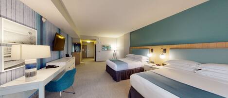 A hotel room with a desk, two beds, a TV, and a lamp.