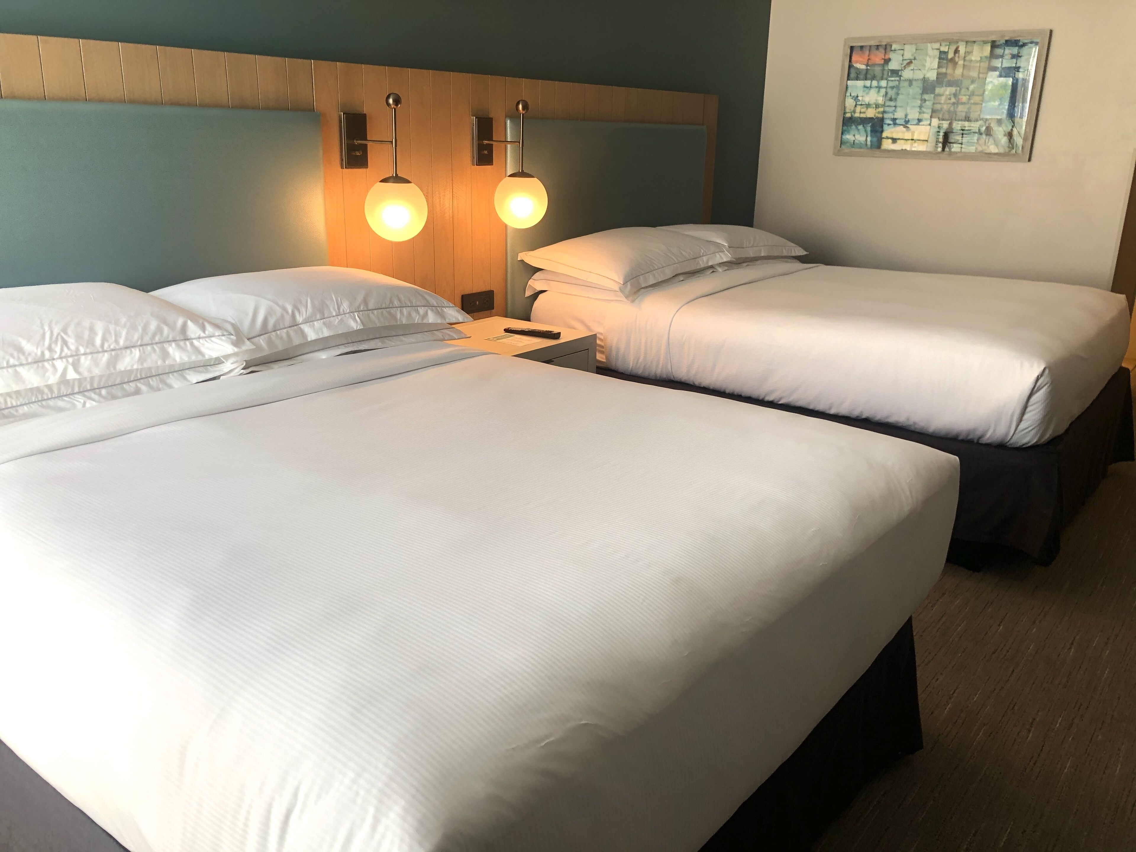 A hotel room with two beds, a wooden headboard, a nightstand, and a wall-mounted artwork.