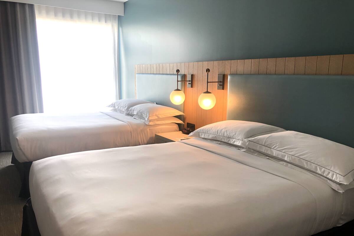 A hotel room with two beds, a wooden headboard, and a wall-mounted lamp.