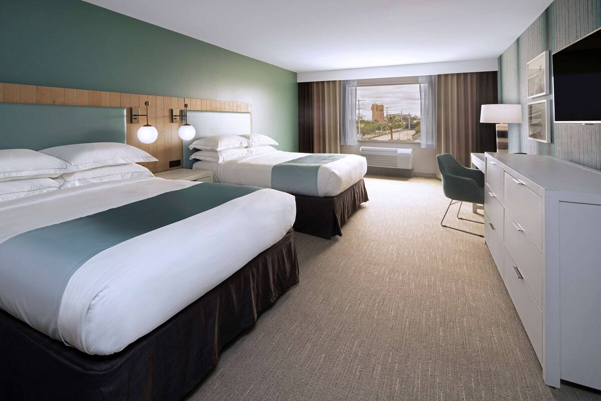 A hotel room with two beds, a desk, and a TV.