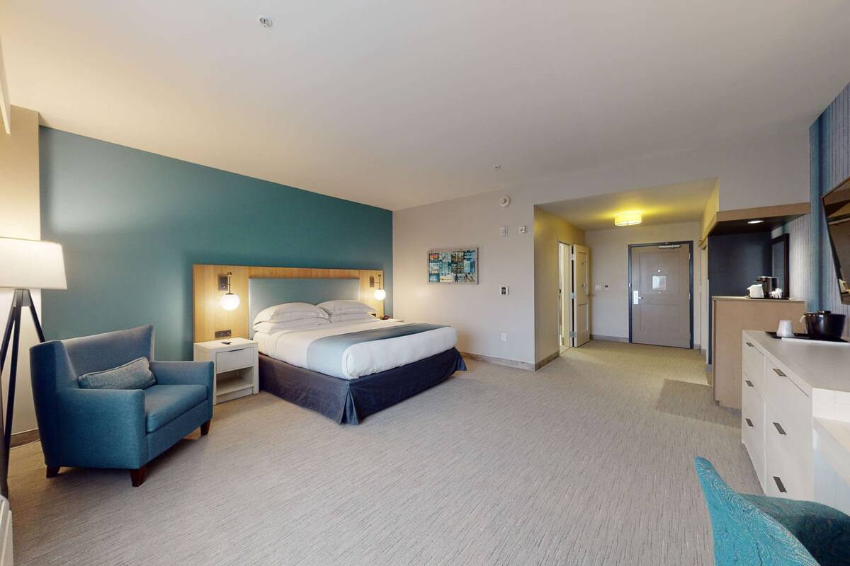 A hotel room with a bed, a desk, a chair, and a dresser.