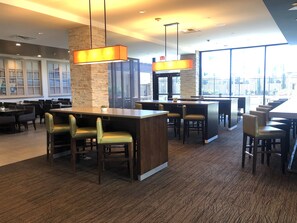 A modern restaurant with high tables, bar seating, and large windows offering city views.