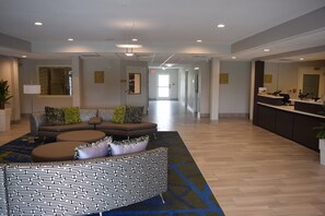 Un hall d’hôtel comprenant un comptoir d’accueil, un espace salon avec un pouf à motifs et un couloir menant aux autres chambres.