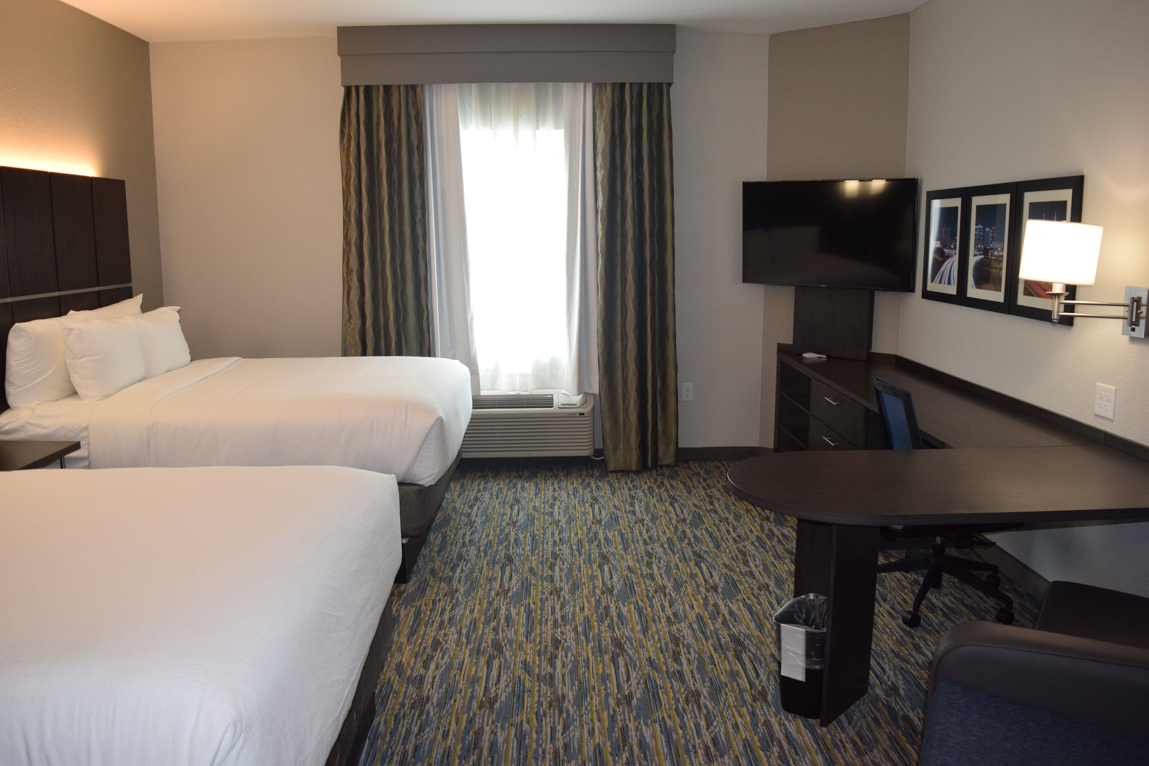 A hotel room with two beds, a desk, a TV, and a window with curtains.