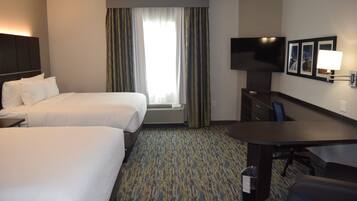 A hotel room with two beds, a desk, a TV, and a window with curtains.