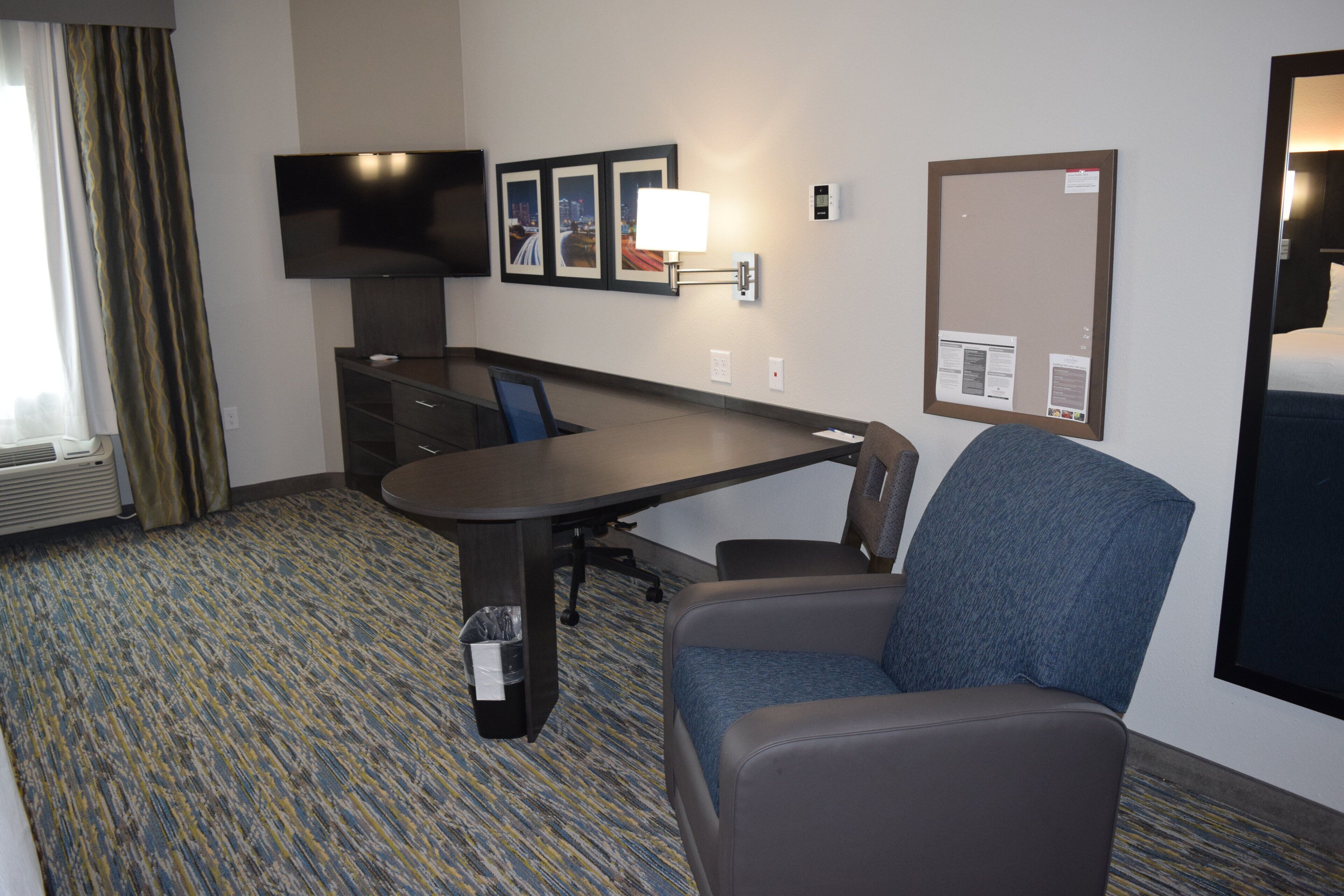 A hotel room with a desk, chair, television, framed pictures, and a mirror.
