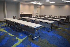 A conference room with multiple tables and chairs, carpeted flooring, and a kitchenette area. - Candlewood Suites Nashville - Metro Center by IHG (Nashville)