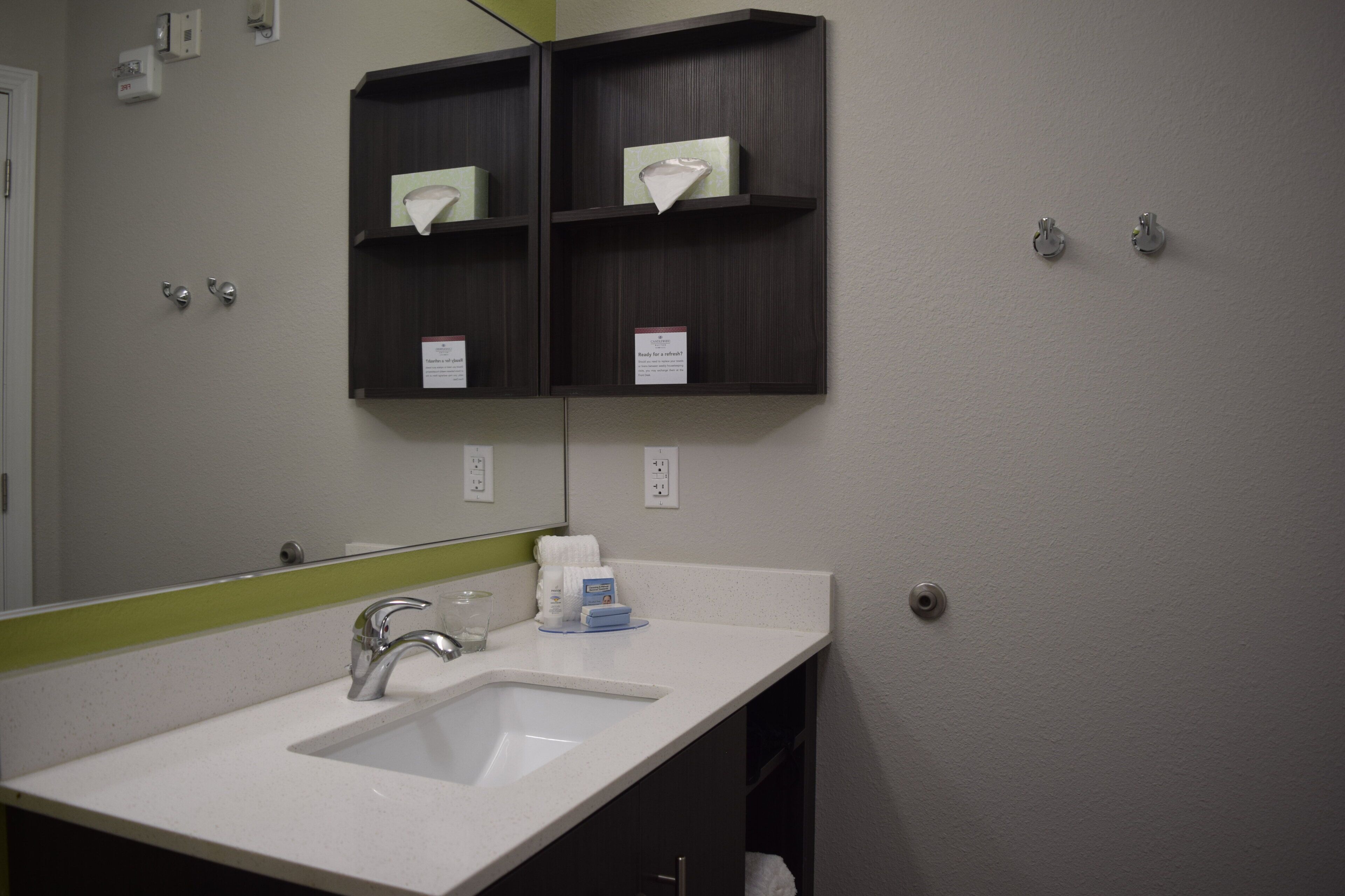 A bathroom with a white sink, a mirror, and a dark wooden shelf above the sink.