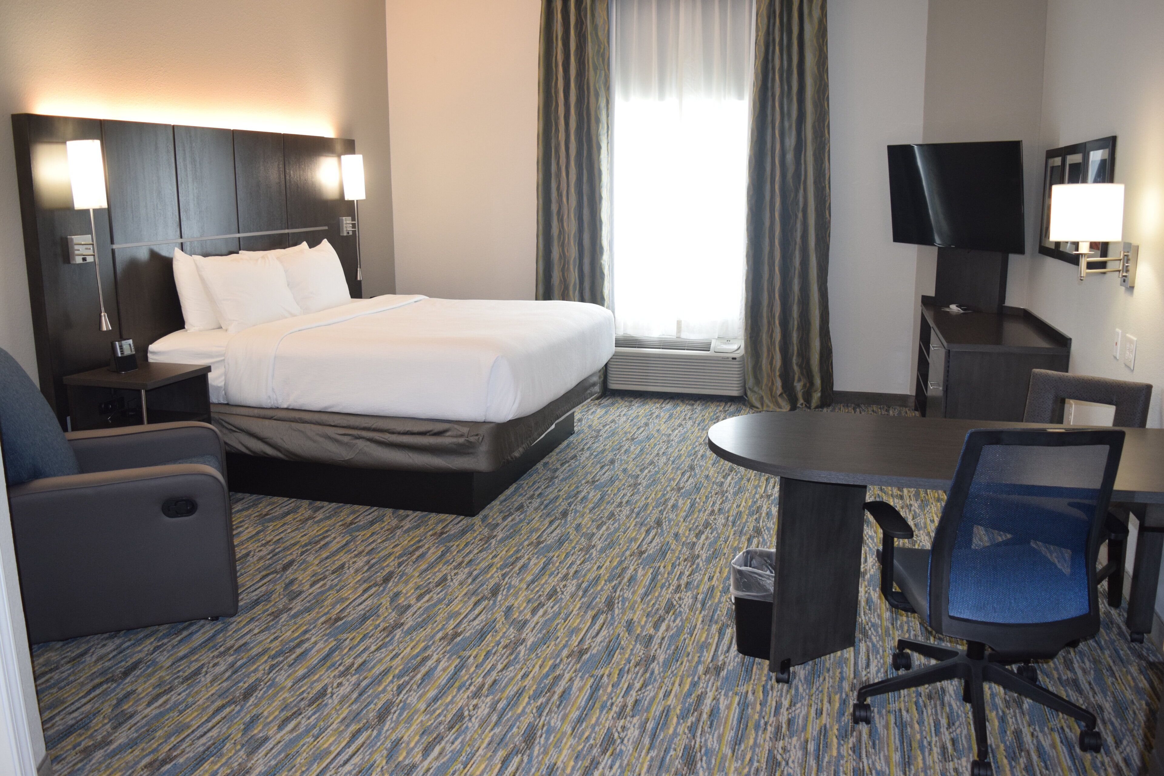 A hotel room with a bed, desk, chair, TV, and lamps.