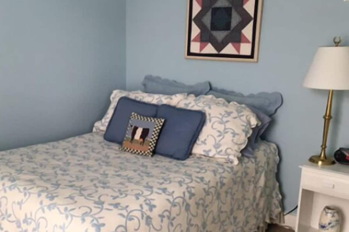 A bedroom with a bed, a bedside table, a lamp, and a wall decoration.