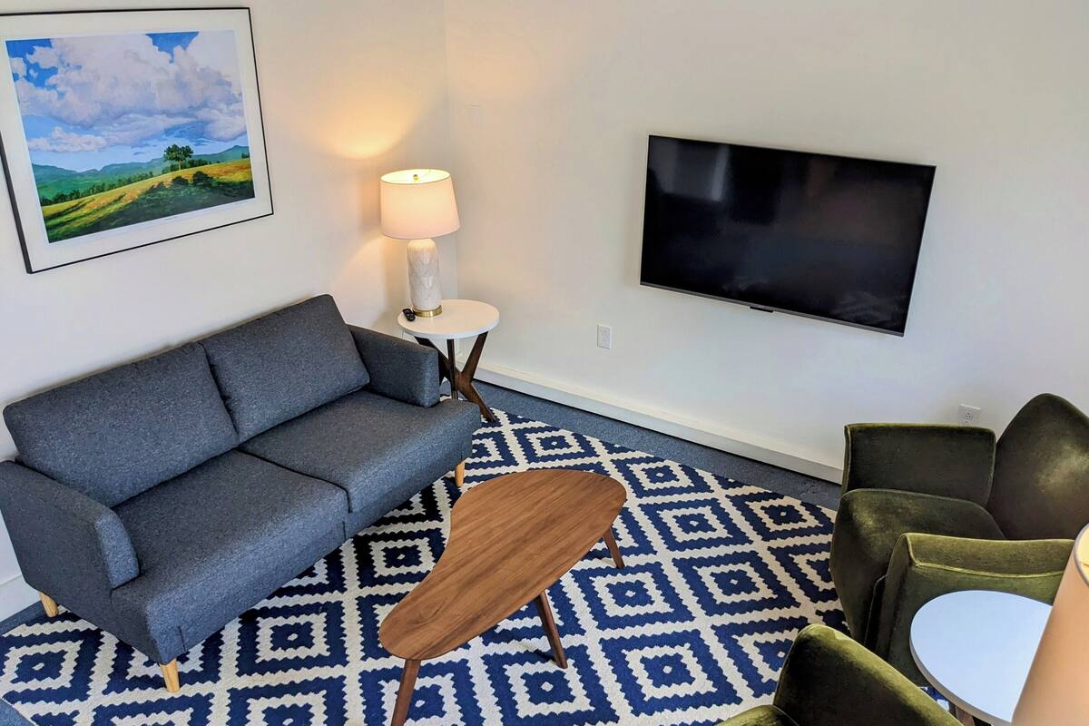 A living room with a grey sofa, a small round table, a lamp, a TV, and a patterned rug.