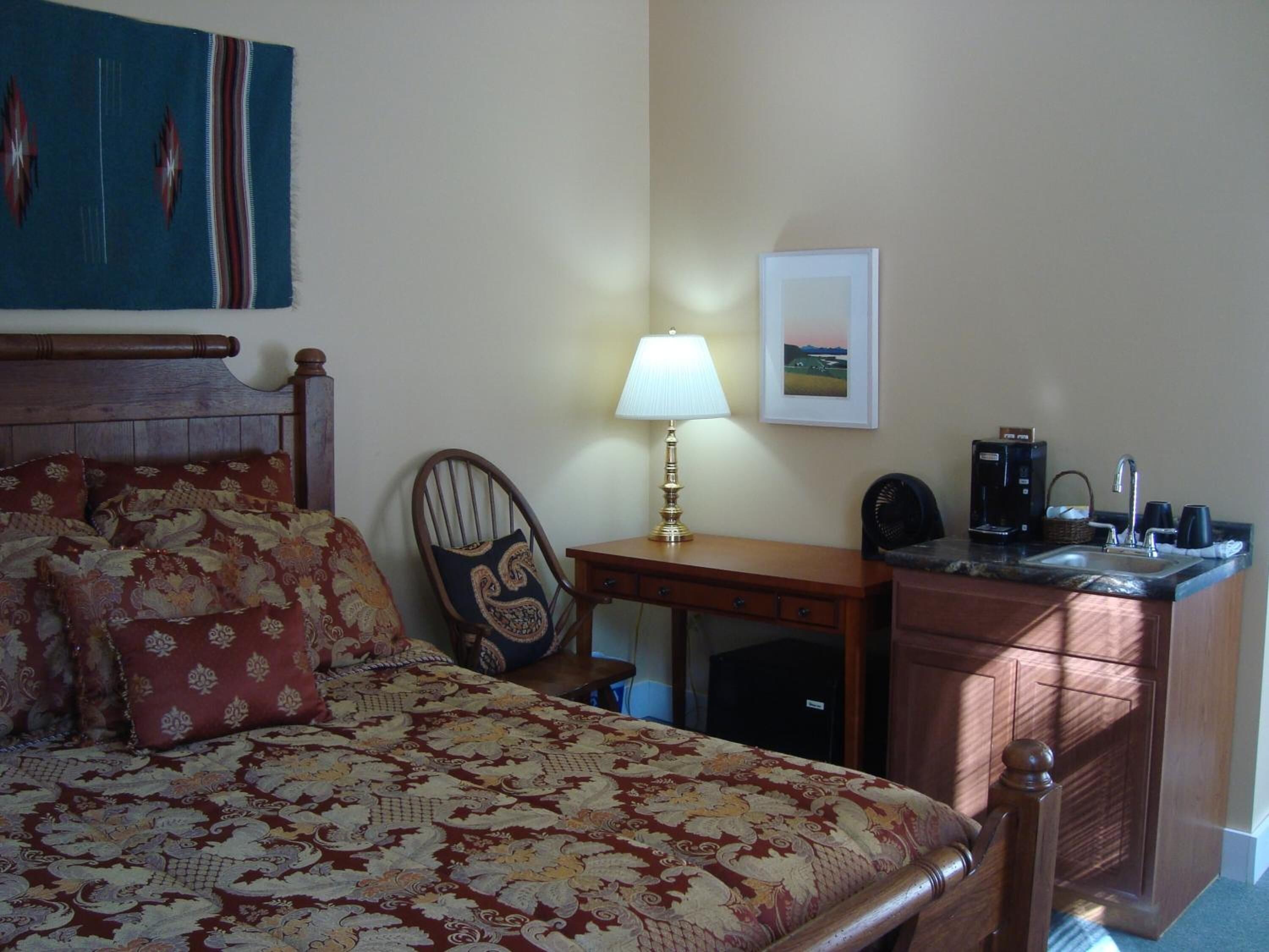 Een hotelkamer met een bed, een bureau, een stoel, een lamp, een koffiezetapparaat en een wastafel.