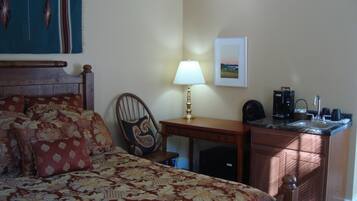 Een hotelkamer met een bed, een bureau, een stoel, een lamp, een koffiezetapparaat en een wastafel.