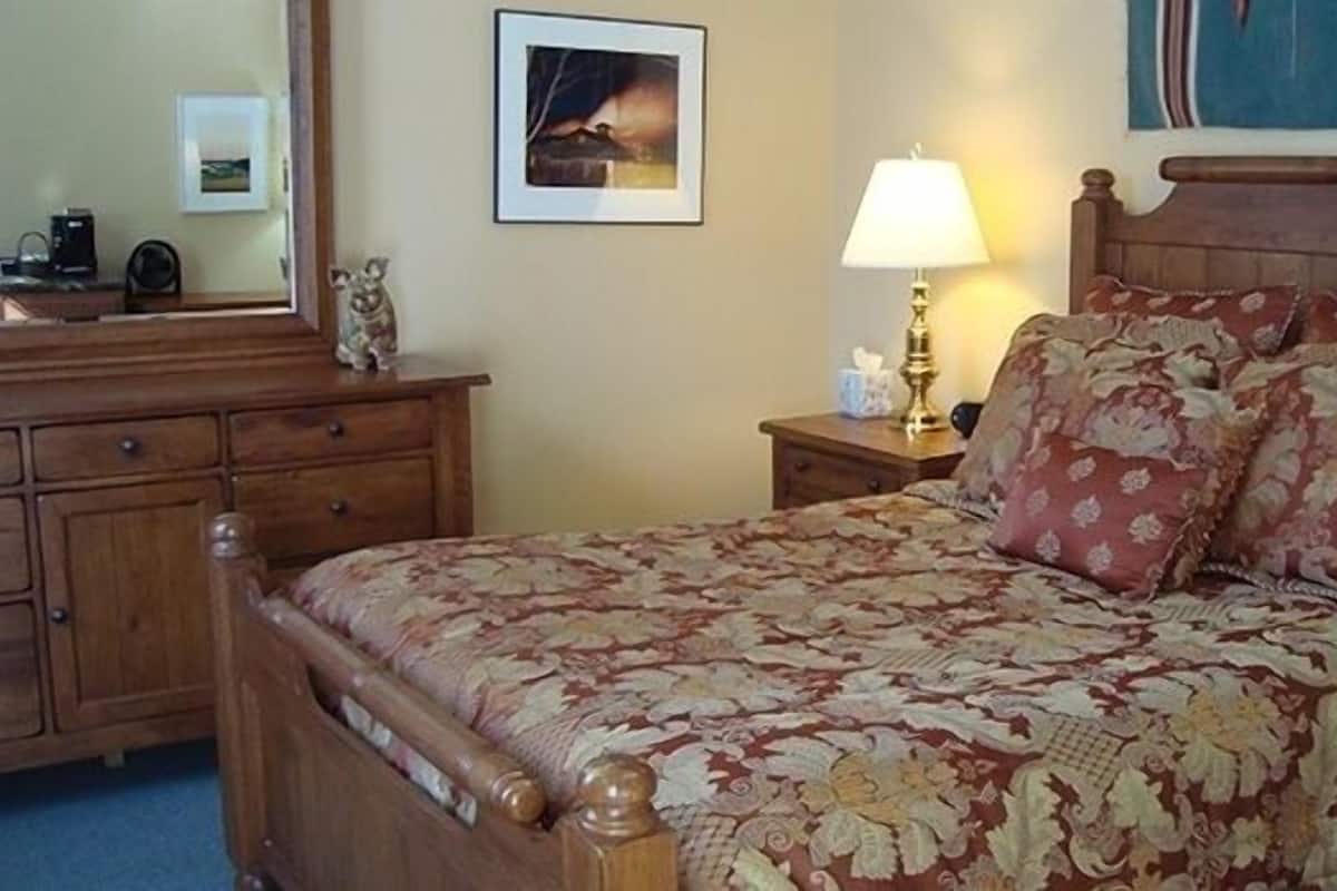 A neatly made bed with floral bedding, a wooden headboard, and a bedside table with a lamp.