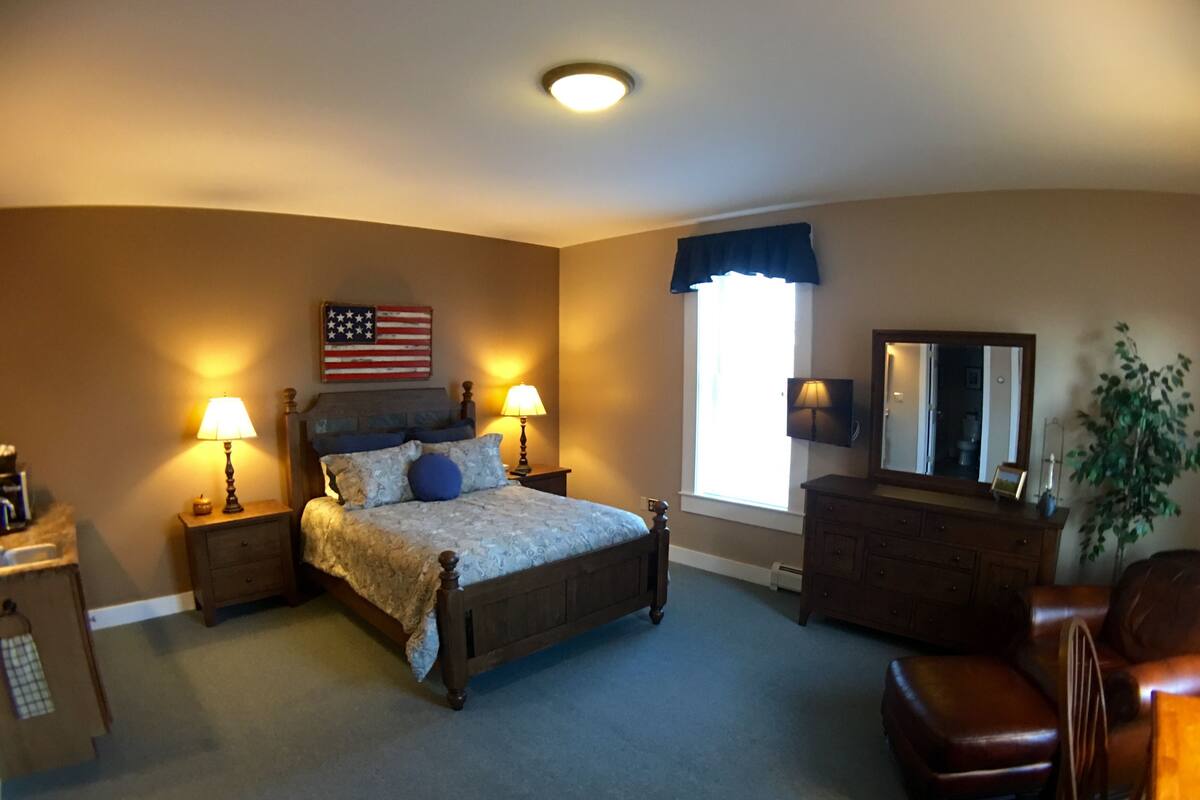 A bedroom with a bed, nightstands, a dresser, a chair, a window with a view, and an American flag on the wall.